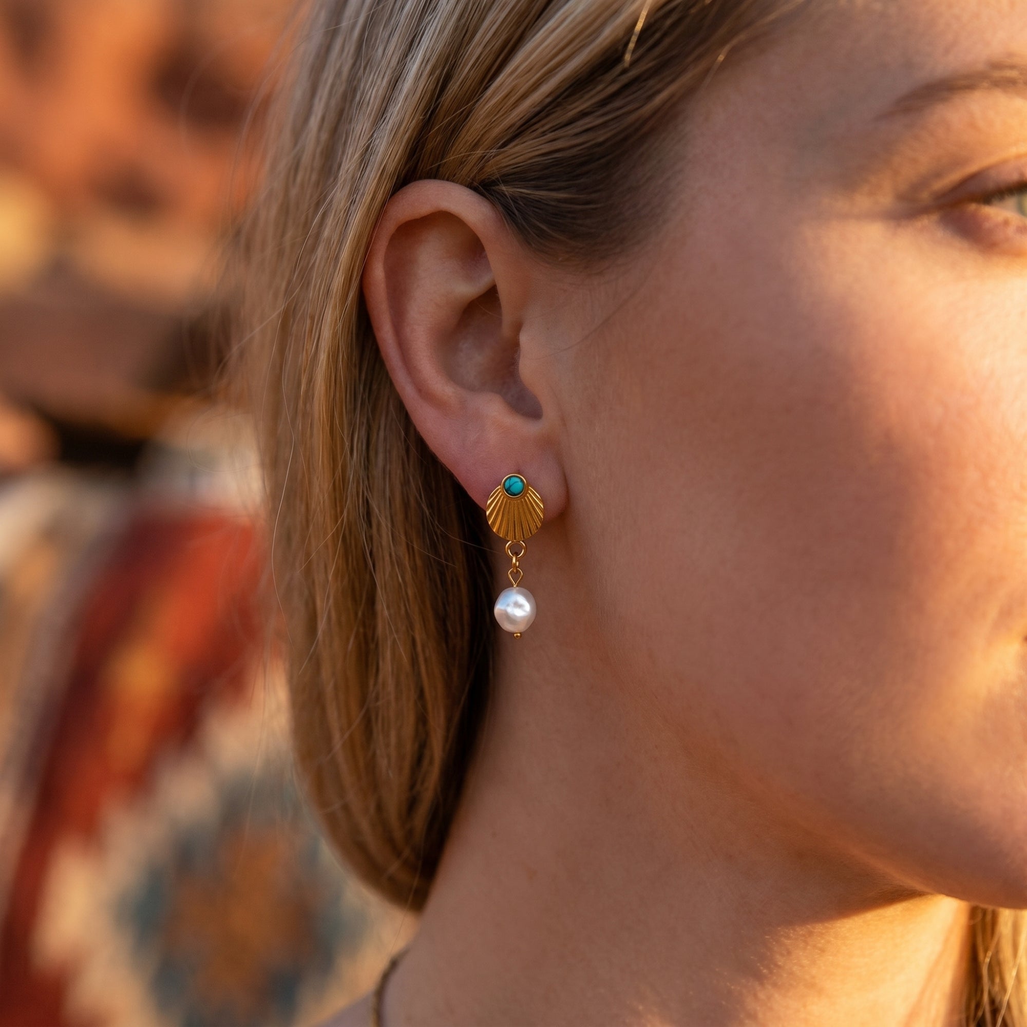 Side profile of a woman wearing a gold shell drop earring with a turquoise bead and dangling white pearl.