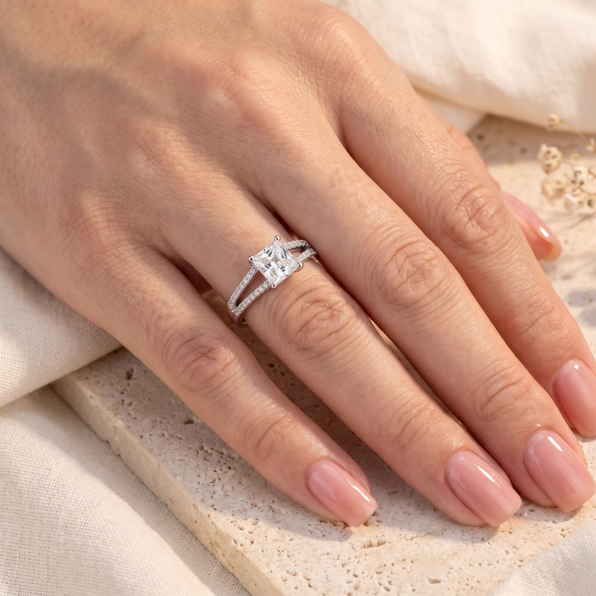 Silver split-shank solitaire ring with a princess-cut center stone worn on a hand resting flat.