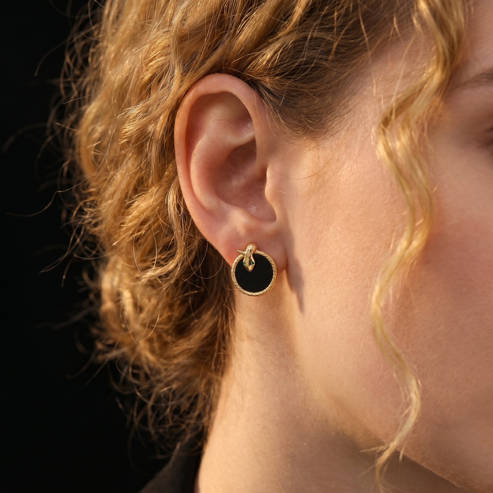 Side view of a model wearing the 18K gold plated Serpens onyx stud earring with a textured snake border.
