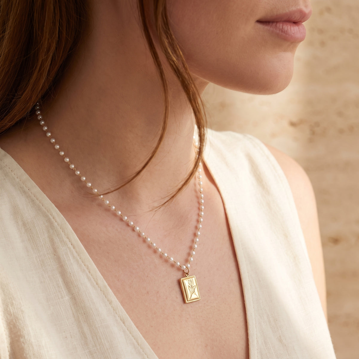 Side view of a model wearing the gold tulip rectangular pendant and white pearl beaded chain with a white top.