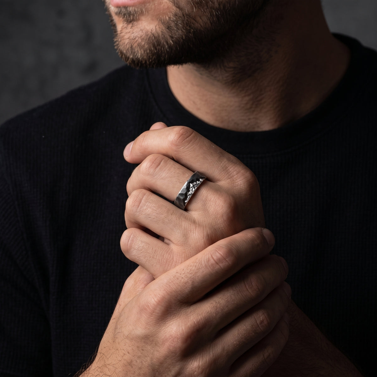A man with clasped hands wears the textured silver mountain ring on one finger.