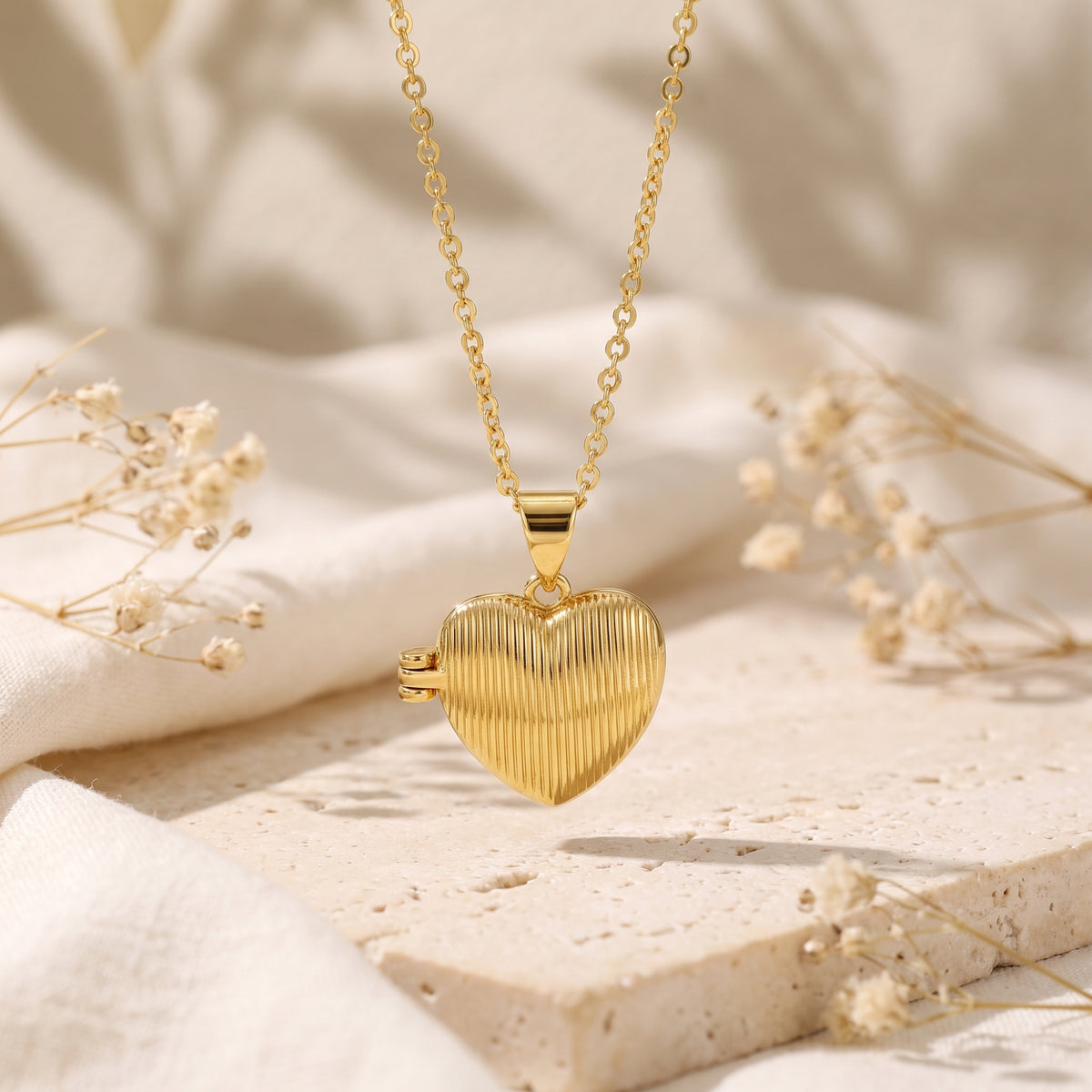 Front view of a gold-tone ribbed heart locket pendant suspended above a light stone slab.
