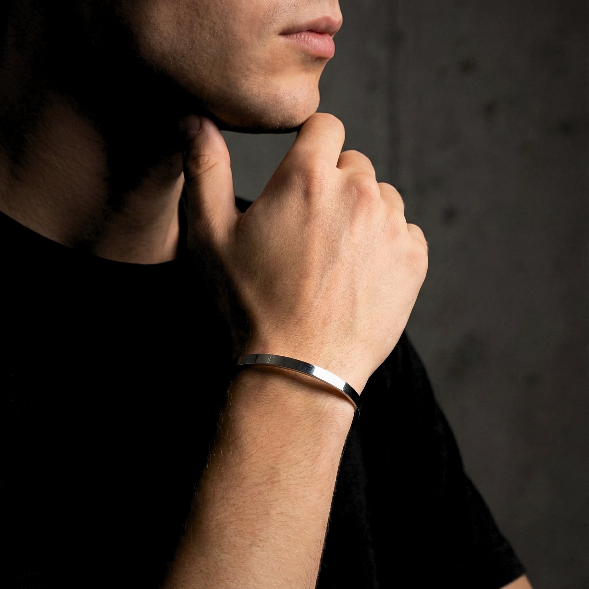 Polished silver stainless steel cuff bracelet for men shown on a model's wrist in a lifestyle pose.