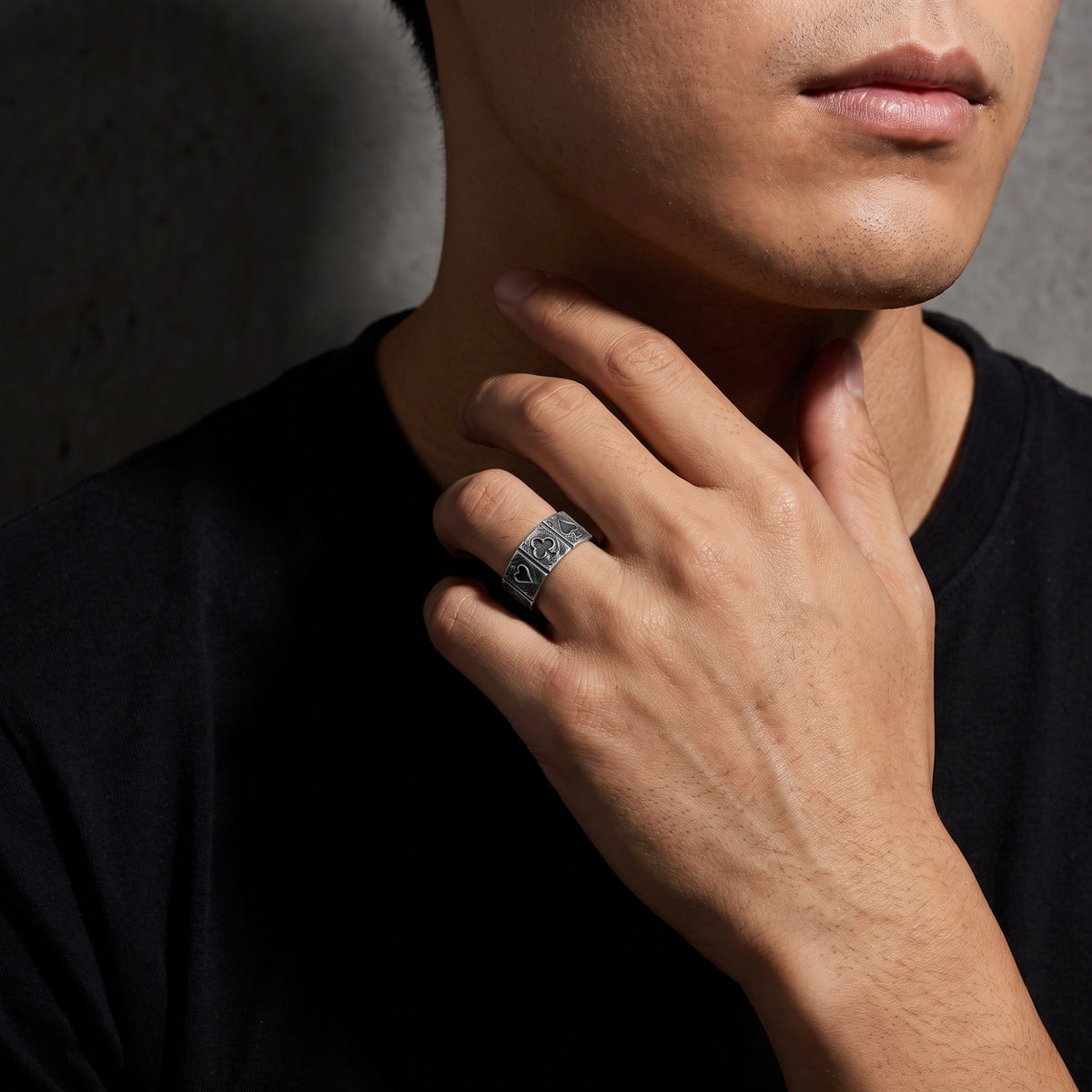 Model wearing the silver four-aces open band ring while touching his neck against a dark wall.