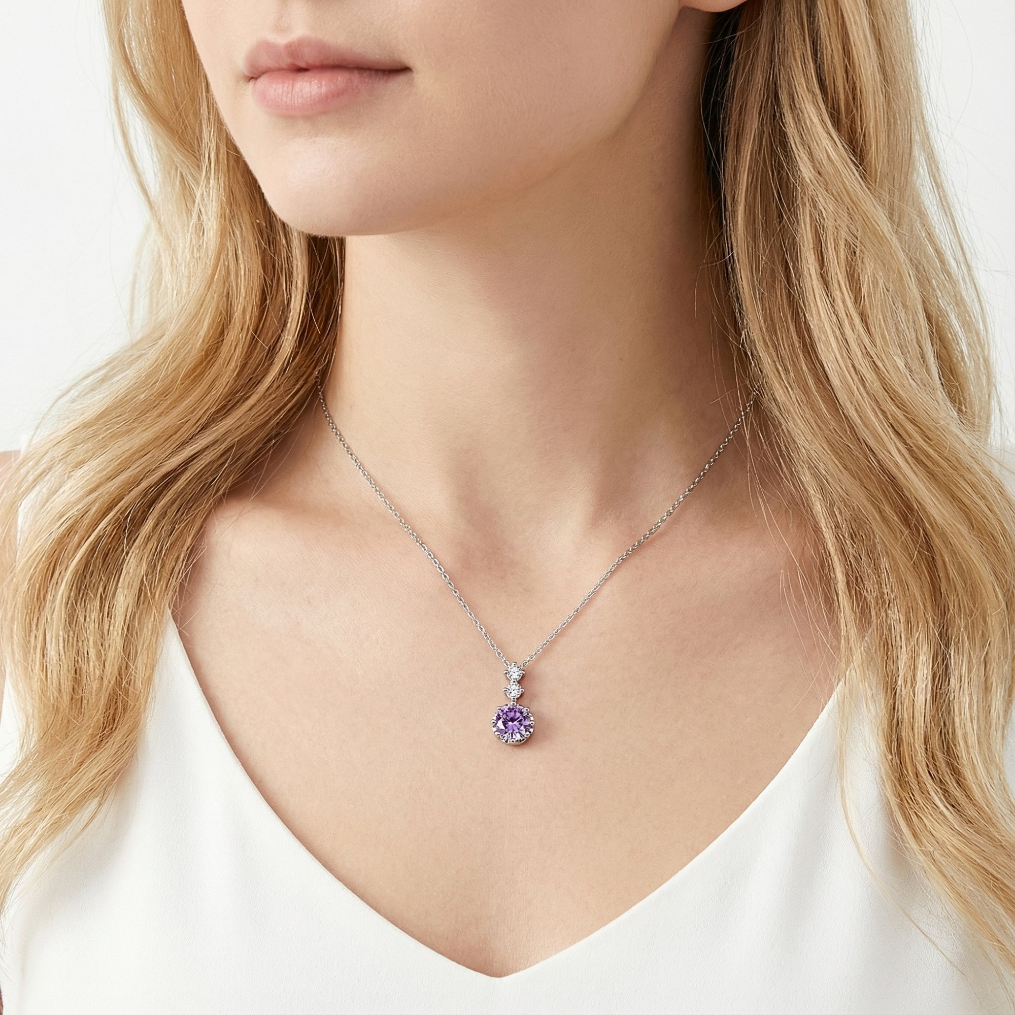 Sterling silver necklace with a round purple birthstone pendant worn by a model in a white top.