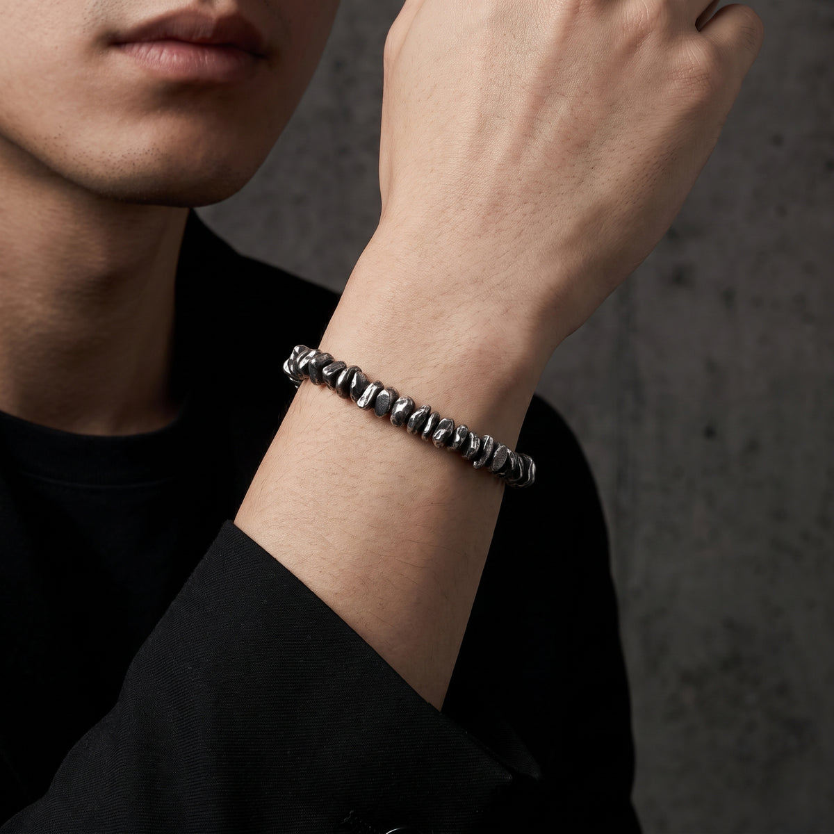 On-model close-up of a raised wrist wearing the silver pebble link bracelet against a dark outfit.
