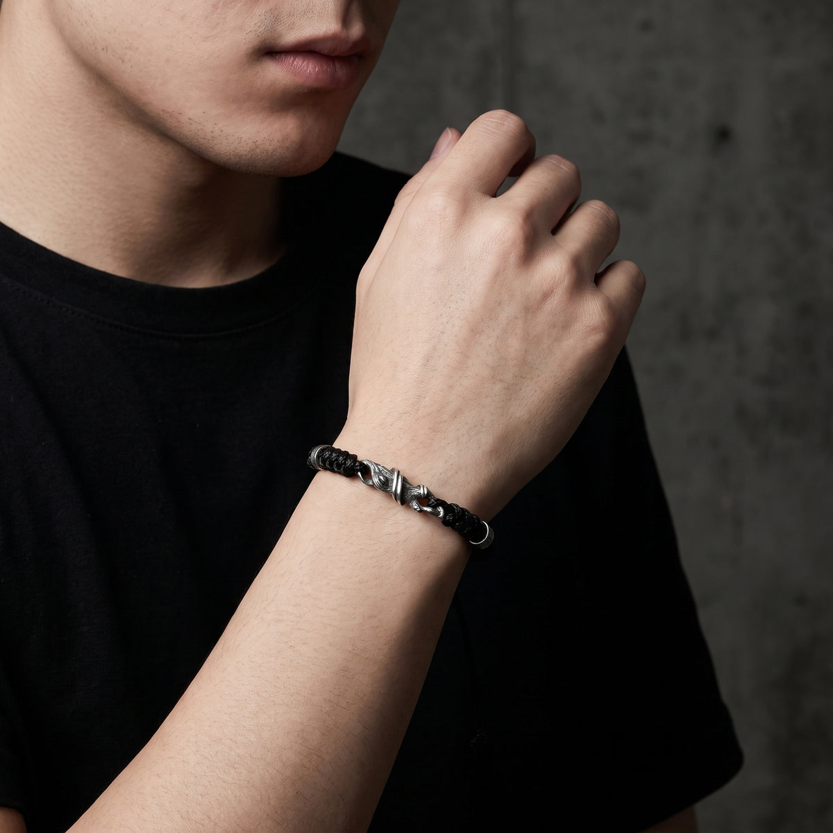 Model wearing the black woven cord bracelet with its silver branch clasp visible against a black T-shirt.