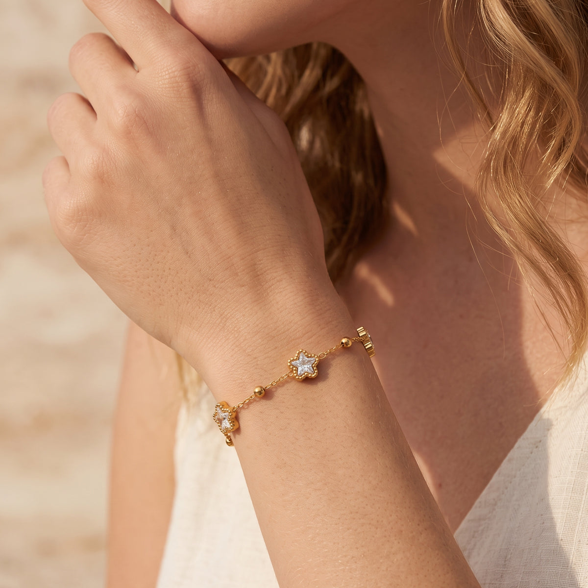 Angled close-up of a woman wearing the gold-tone star station bracelet on her wrist near her face.