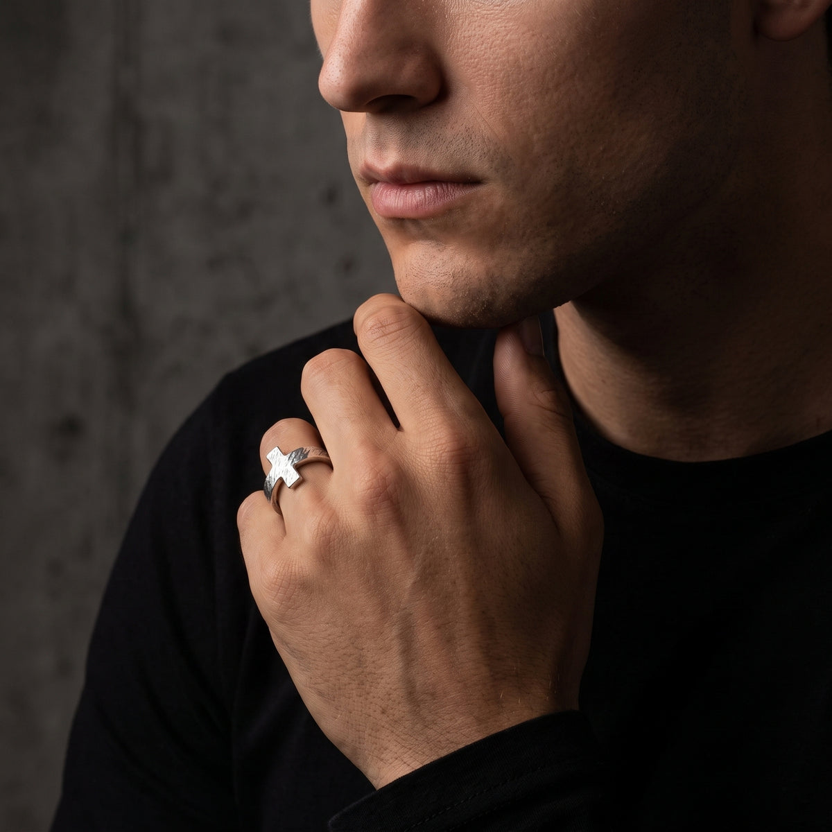 Close-up of a man resting his hand under his chin while wearing the textured cross ring.