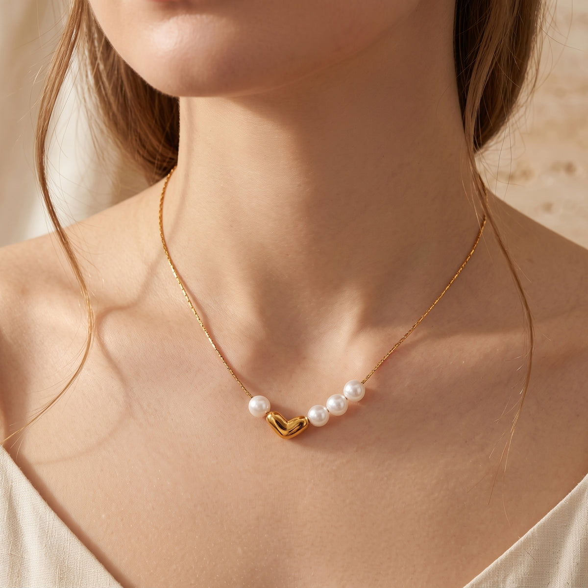 Front view of a model wearing the gold-tone heart and pearl necklace centered at her neckline.