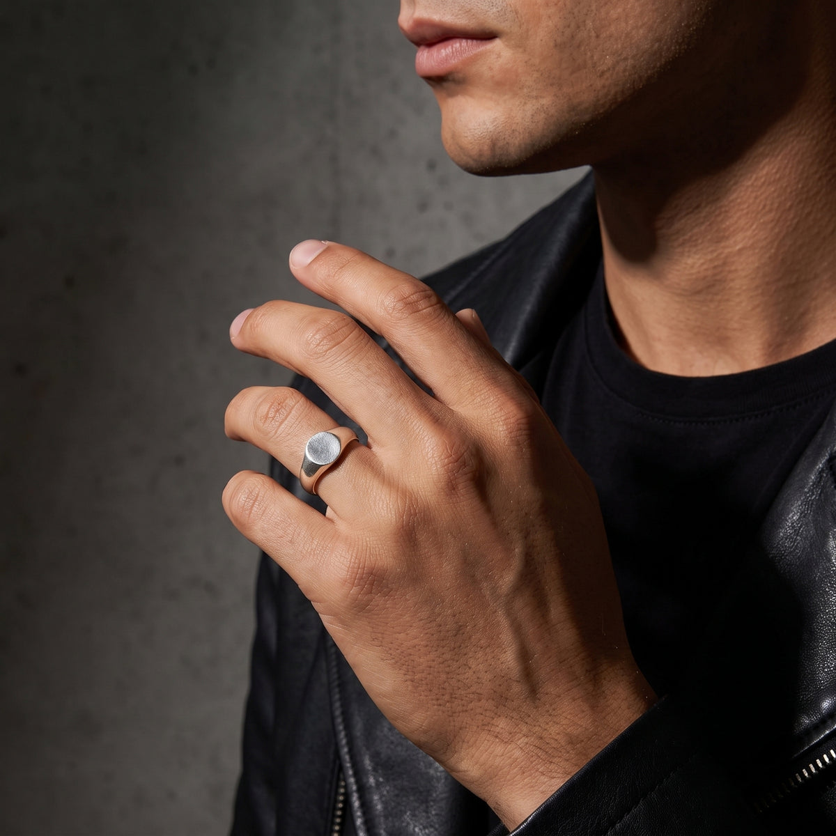 Model wearing the silver ring on a ring finger with a hand raised against a gray wall, dressed in a black leather jacket.