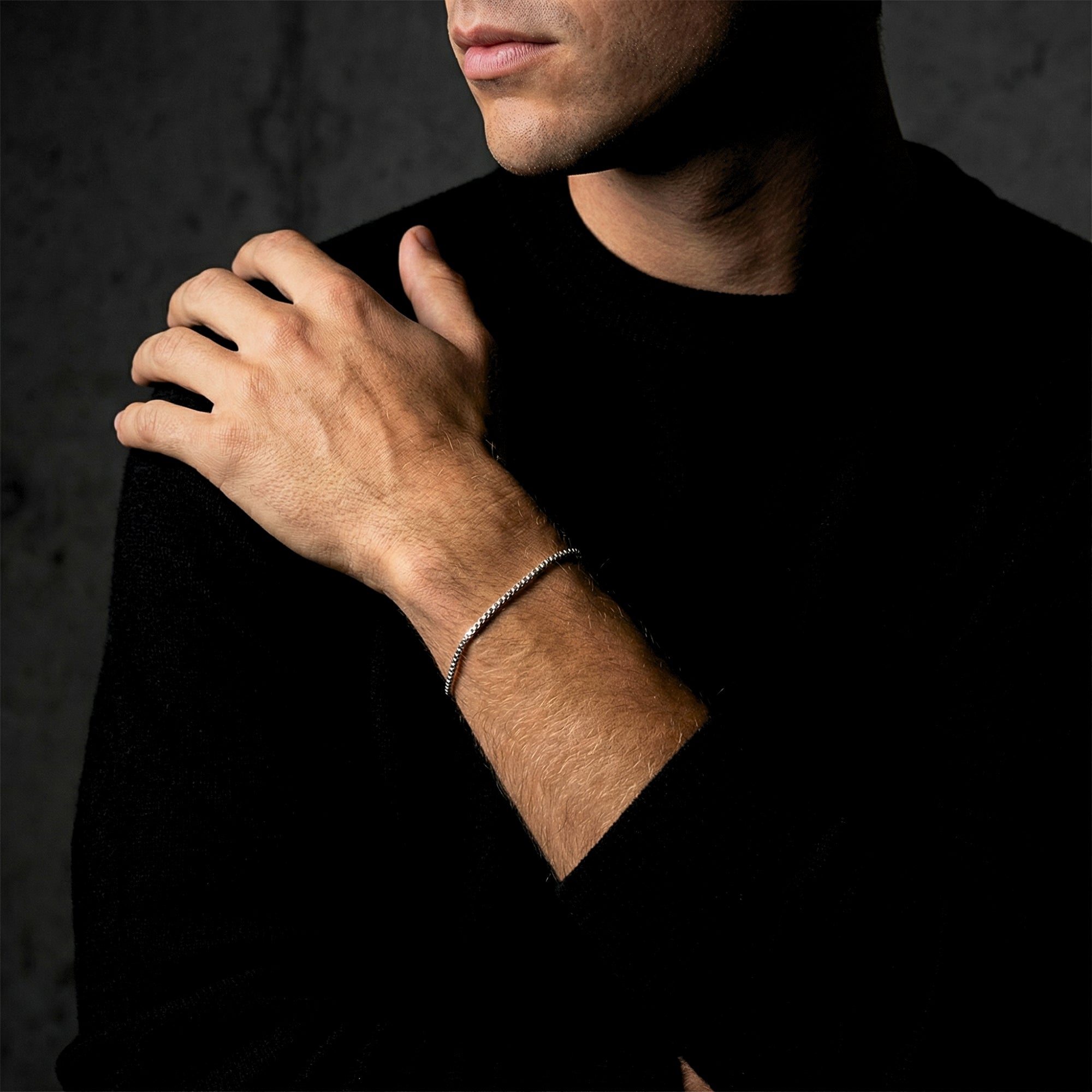 Silver stainless steel box chain bracelet for men styled on a wrist against a dark background.