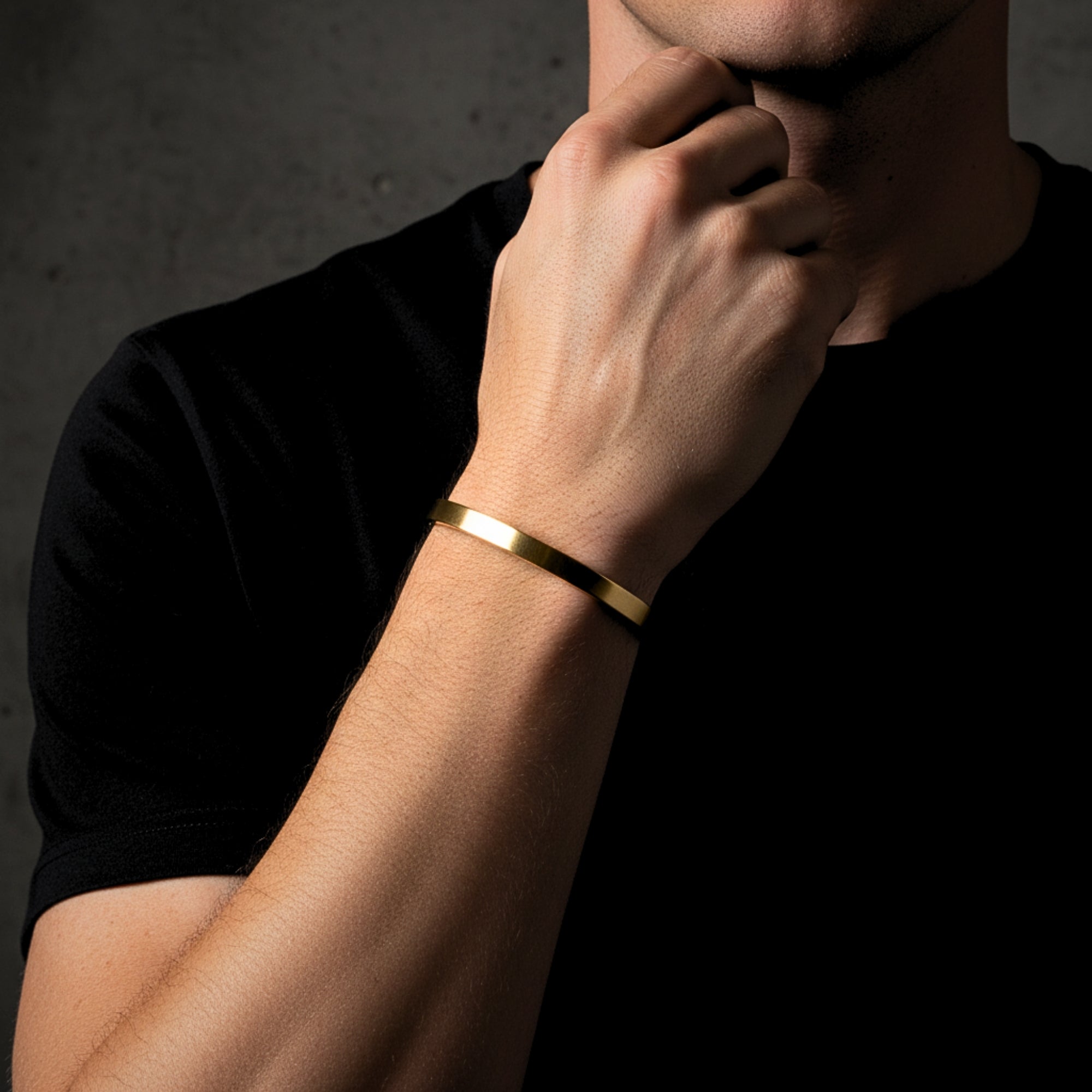 Minimalist gold stainless steel Meridian Cuff bracelet styled on a man's wrist with a black t-shirt.