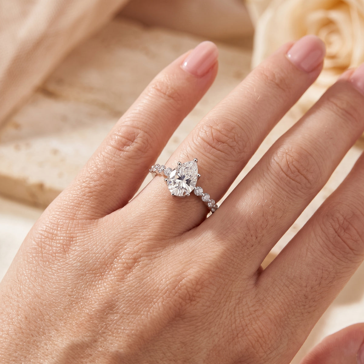 Close-up of the silver ring on a hand, showing the detailed pear-cut center stone and side accent stones.