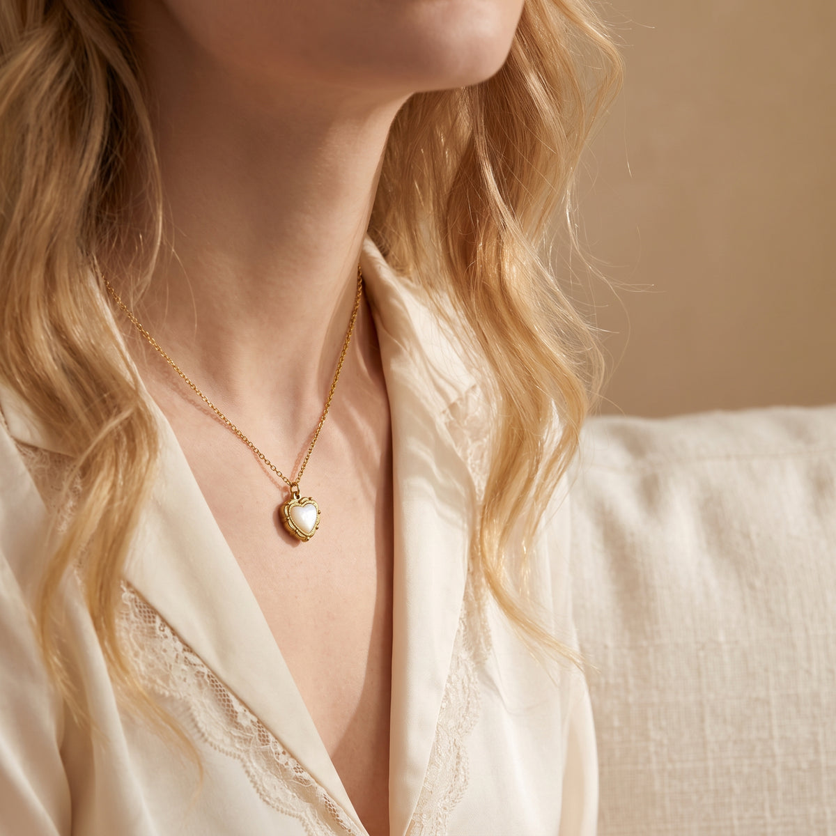 Model wearing the gold-tone heart pendant necklace with a white mother-of-pearl simulant inlay over a lace-trimmed top.