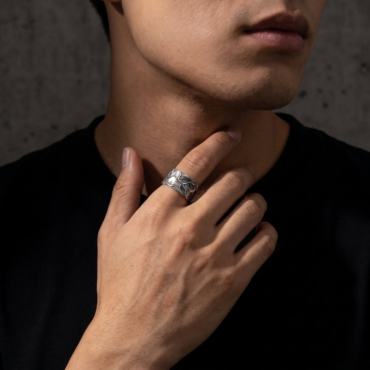 Model displaying the textured silver open band ring on his index finger against his neck.