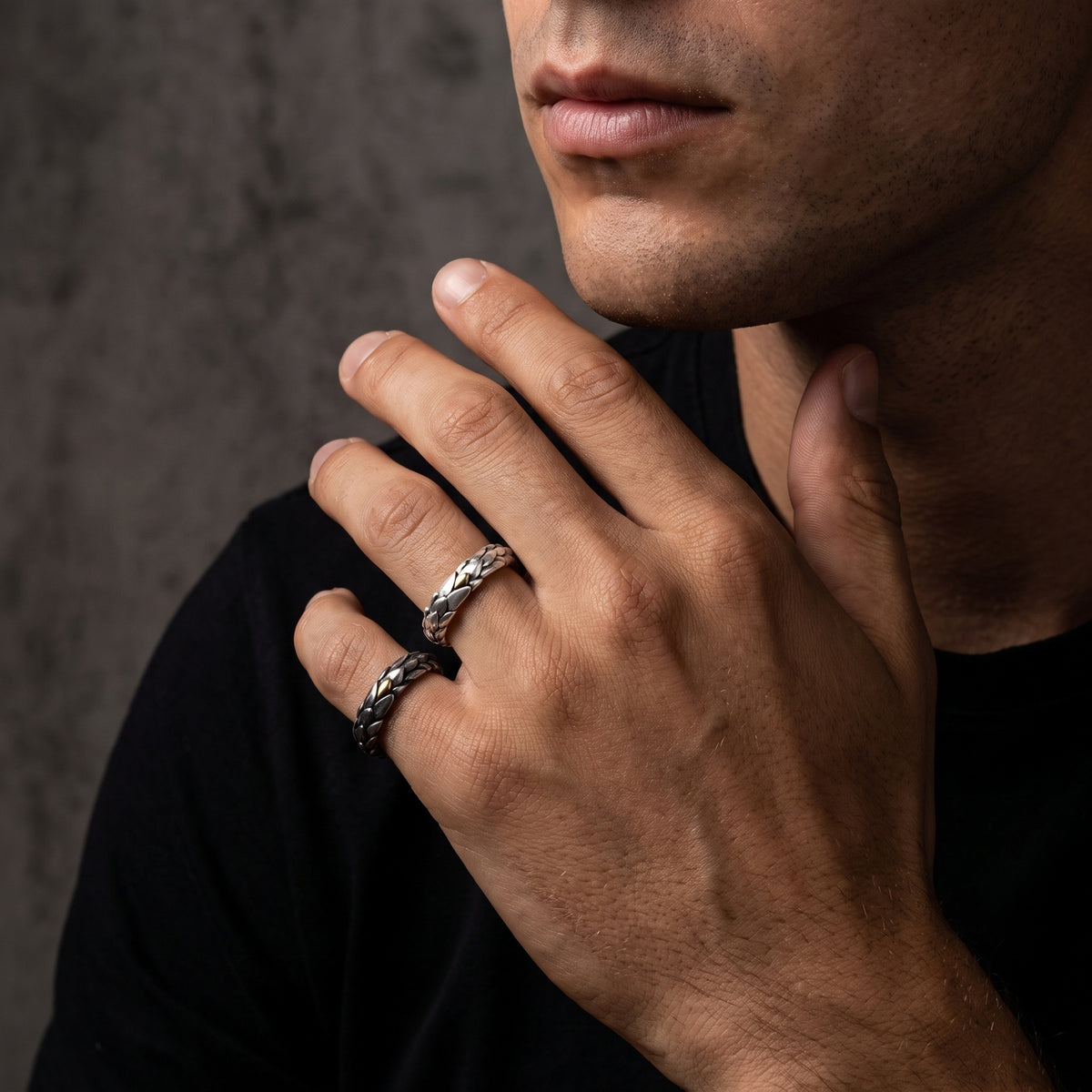 Close view of a man wearing two dragon-scale open rings with gold-colored accents, holding his hand near his chin.