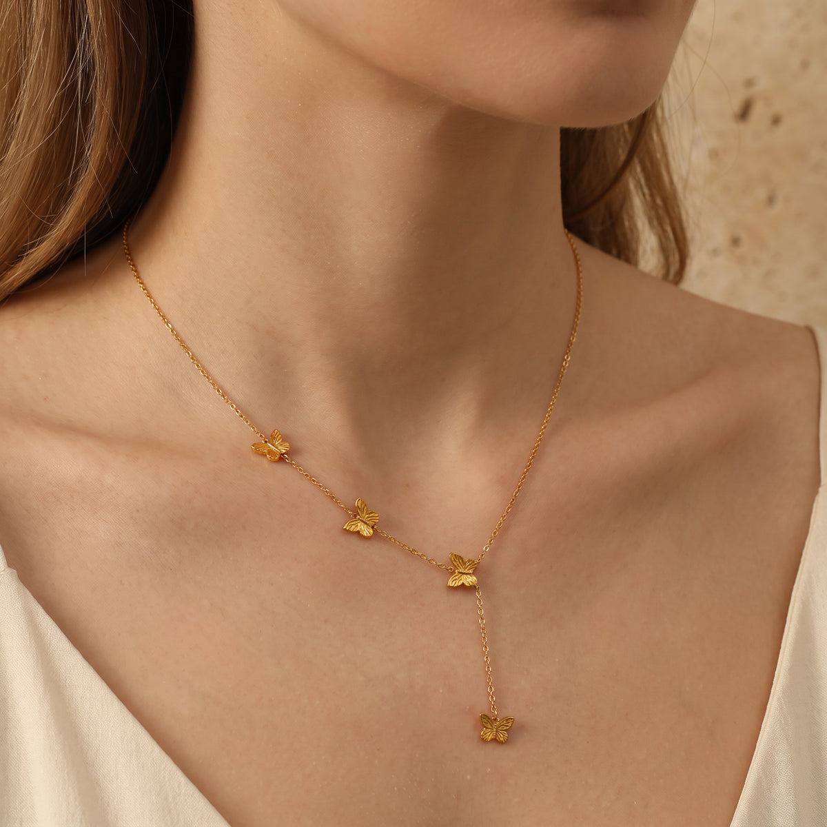 Front view of a model wearing a gold-tone butterfly lariat necklace over a white top.