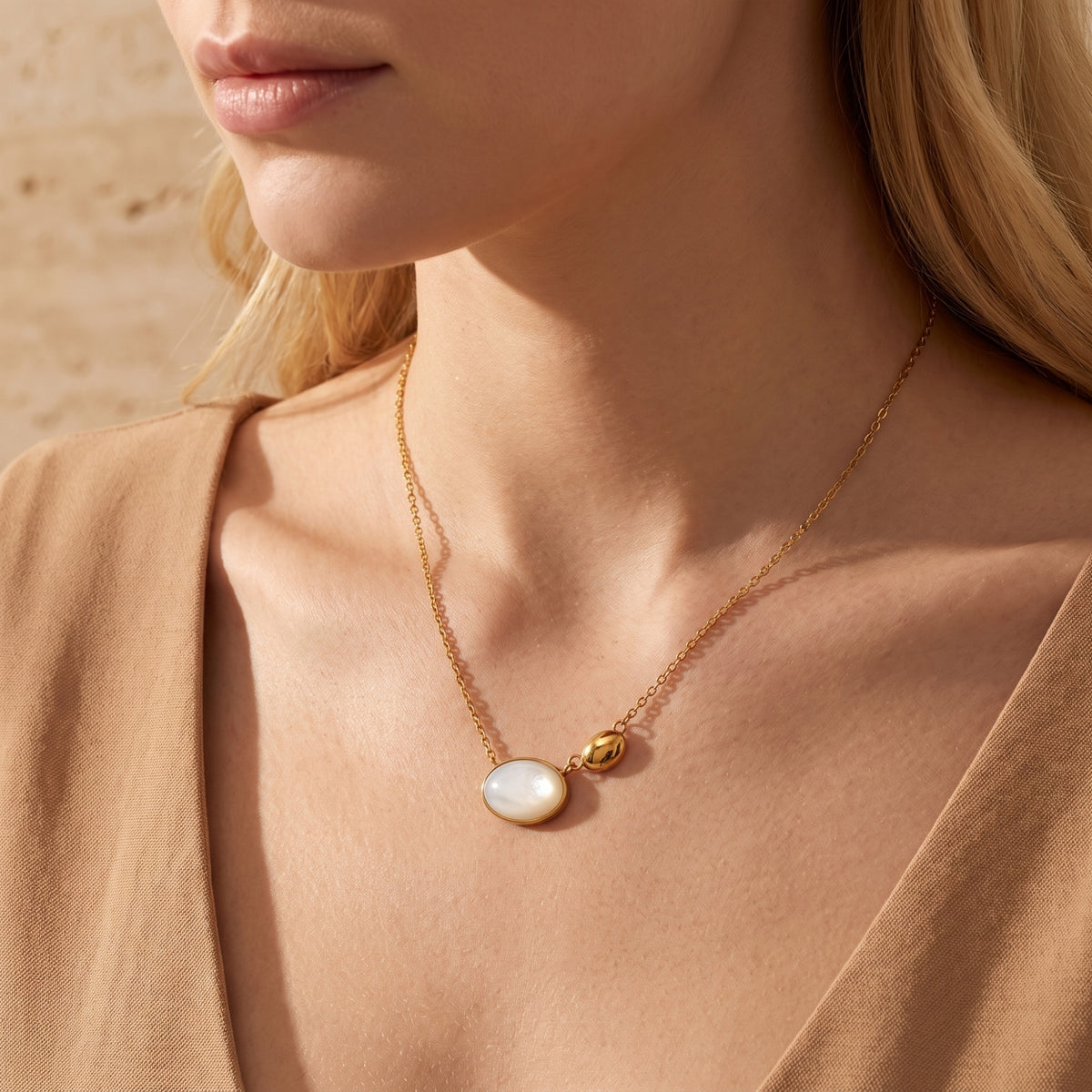 Model wearing a gold-tone mother-of-pearl and pebble pendant necklace with a warm beige outfit.