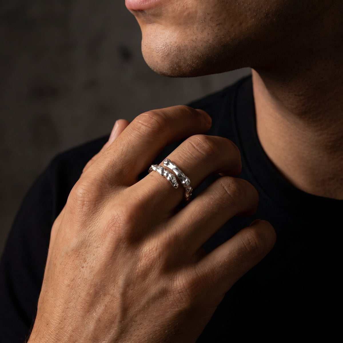 Man wearing the silver molten wrap ring, resting his hand near his jawline in a black top.