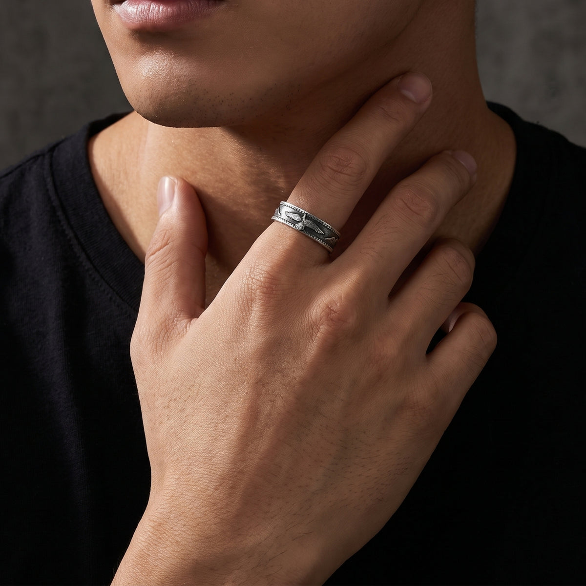 Close-up of a person wearing the silver eagle open-band ring on an index finger with the hand near the neck.