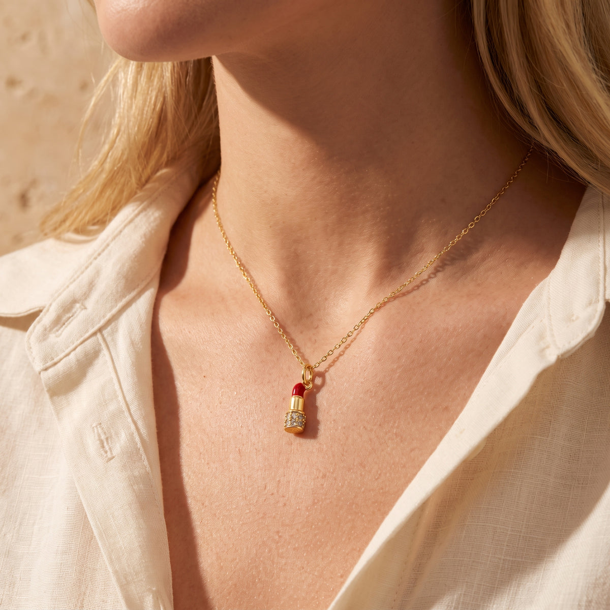 Close-up angled view of a model wearing the gold-tone lipstick necklace against an open white blouse.