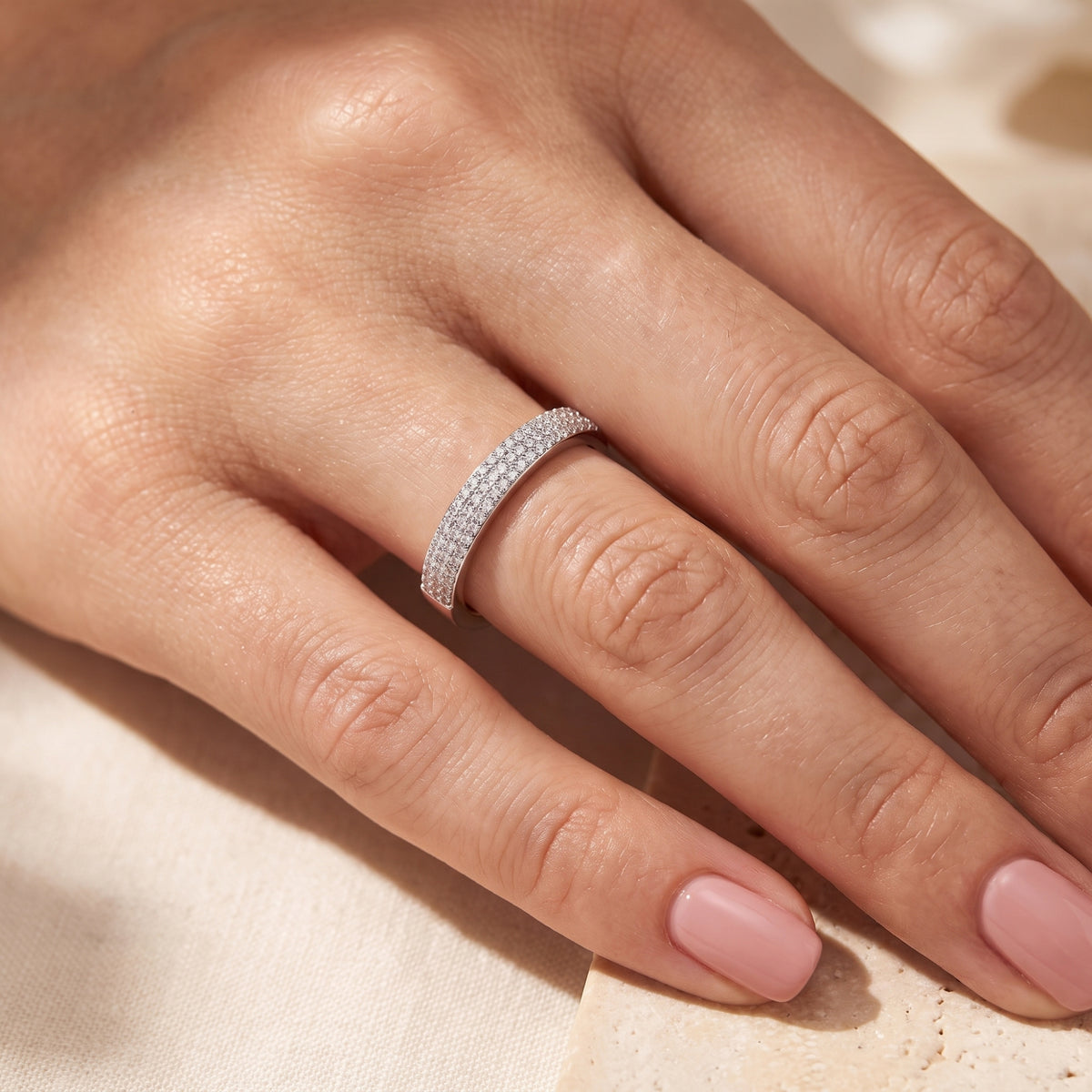 Close-up of a hand wearing a silver band ring with three rows of clear pavé stones.
