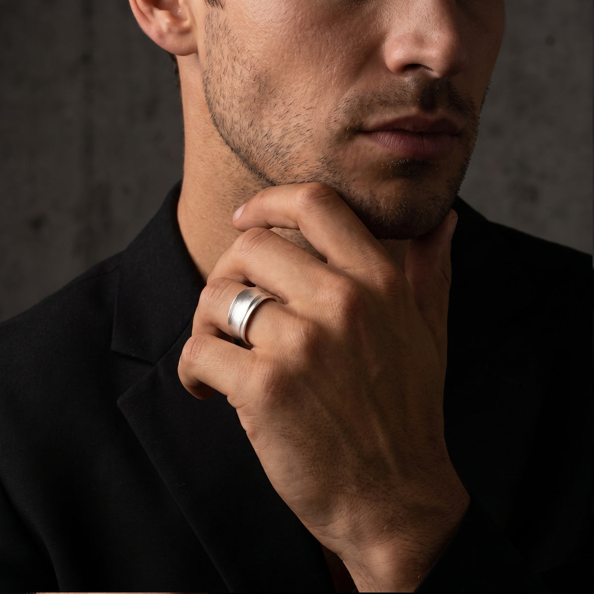 Man wearing a wide brushed silver contour ring with a black jacket.
