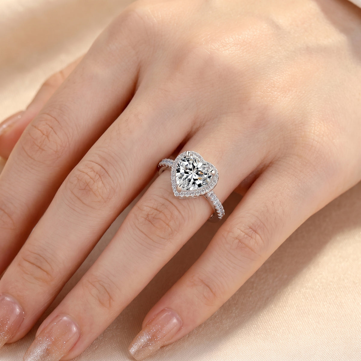 Overhead view of a silver heart-shaped halo ring with a simulated diamond and pavé band worn on a hand.