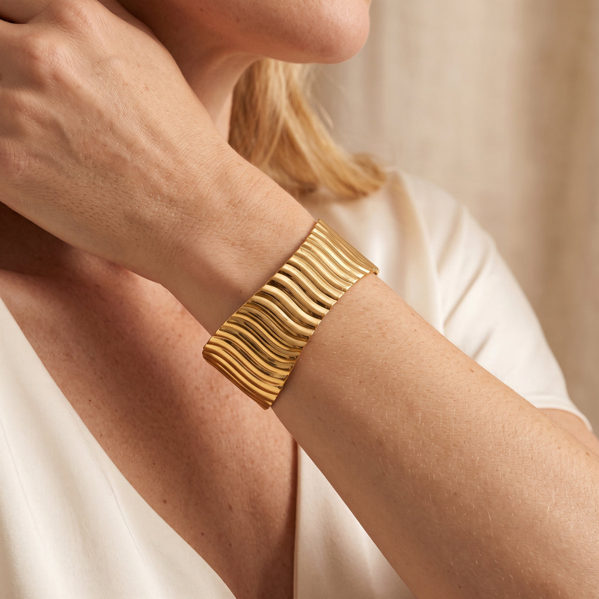 Close-up of a model wearing a wide gold-tone wave cuff bracelet on her forearm.