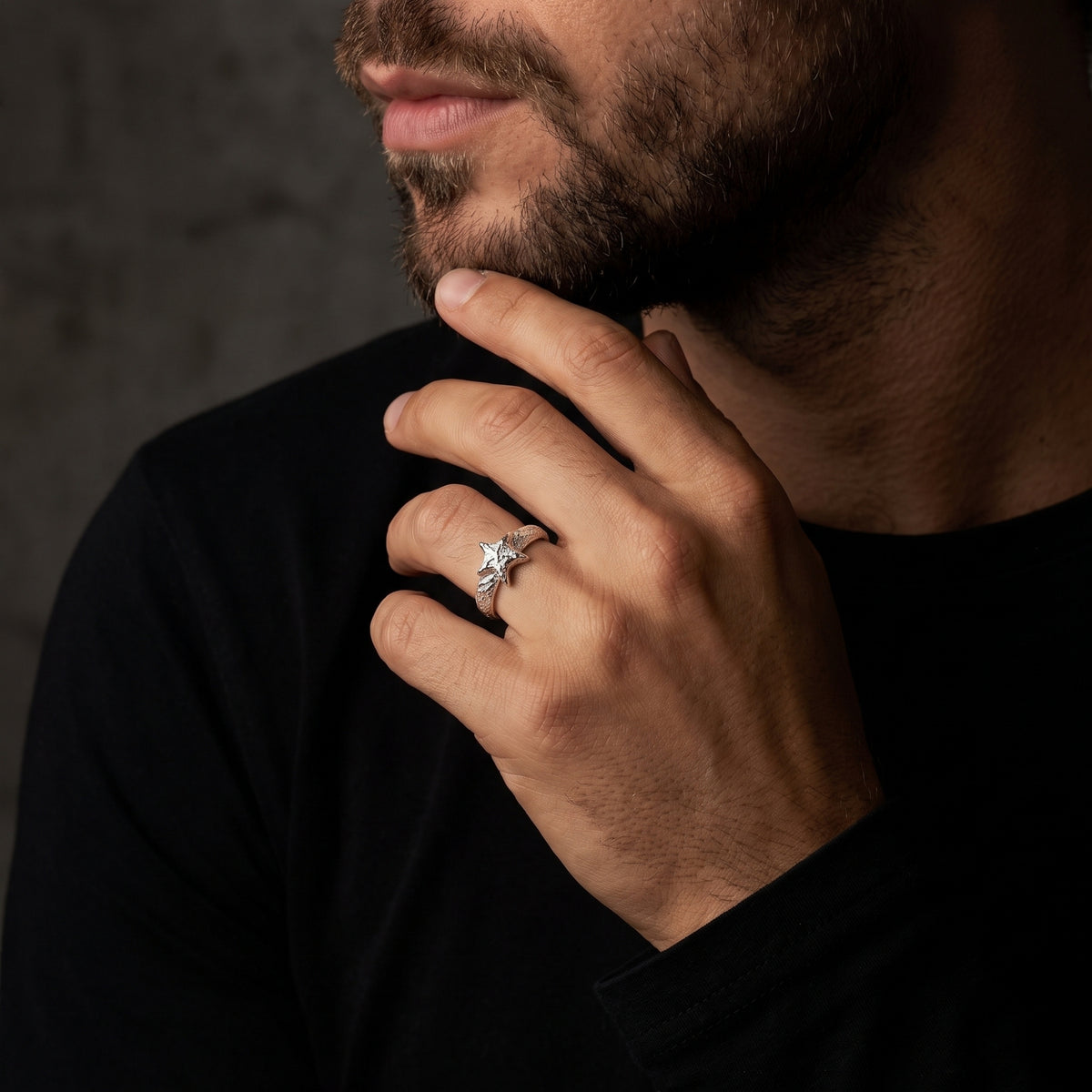 Bearded man in a black top wearing a textured silver star ring on his ring finger.