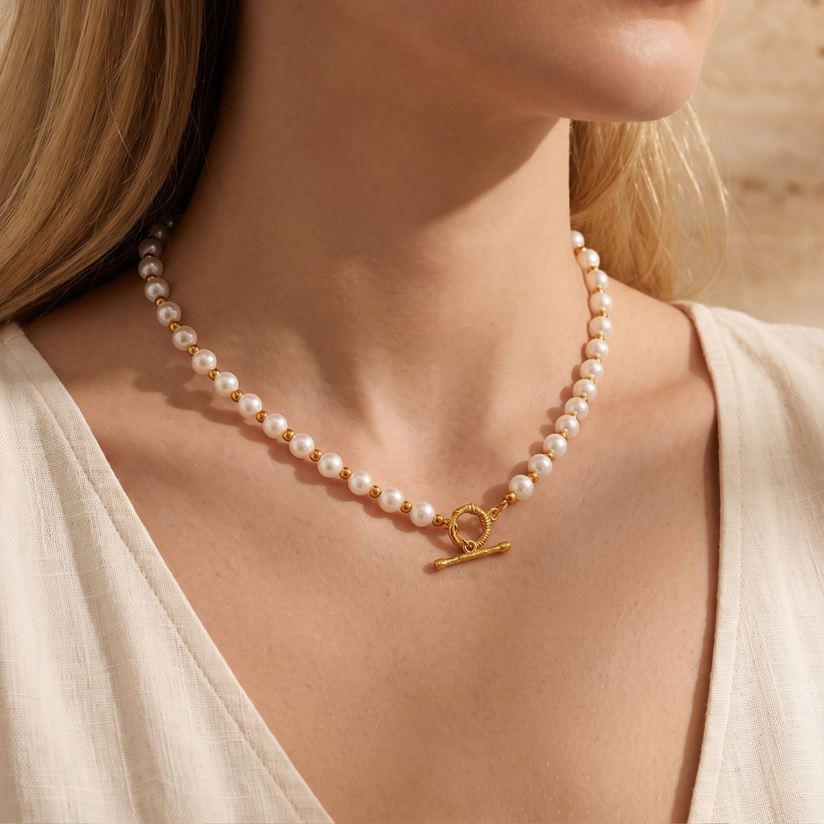 Close view of a white simulated pearl necklace with gold-tone spacer beads and a T-bar toggle clasp worn at the neck.
