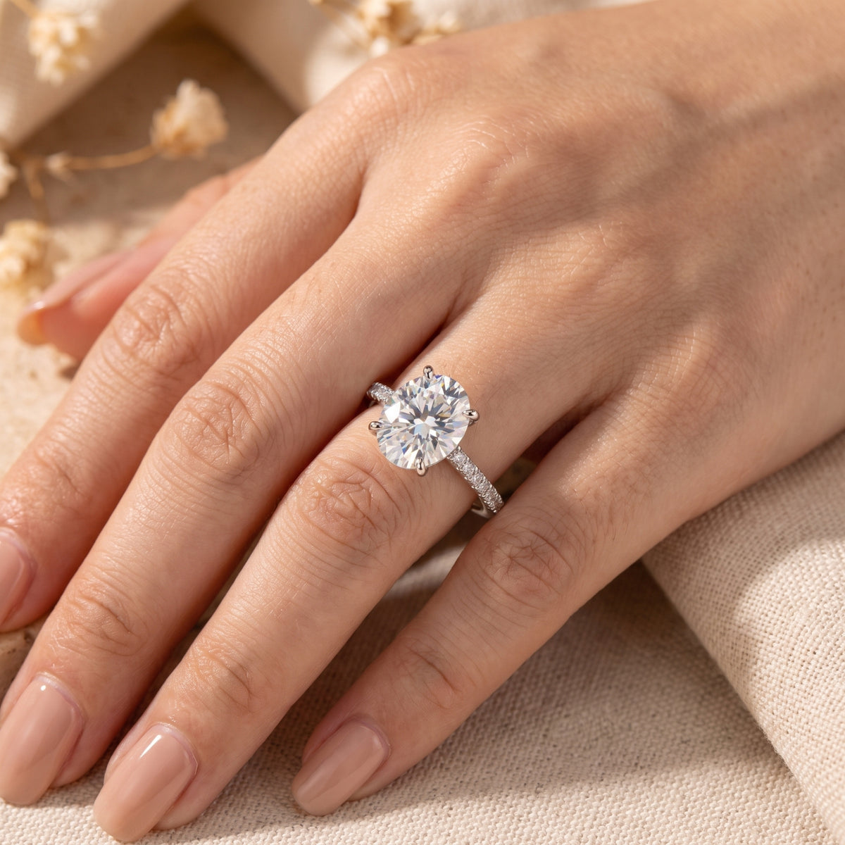 Close-up of the silver oval ring worn on a hand resting against textured fabric.