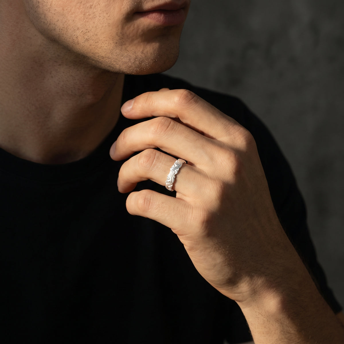 Close-up of the silver wave scroll open ring worn on a ring finger in warm directional light.