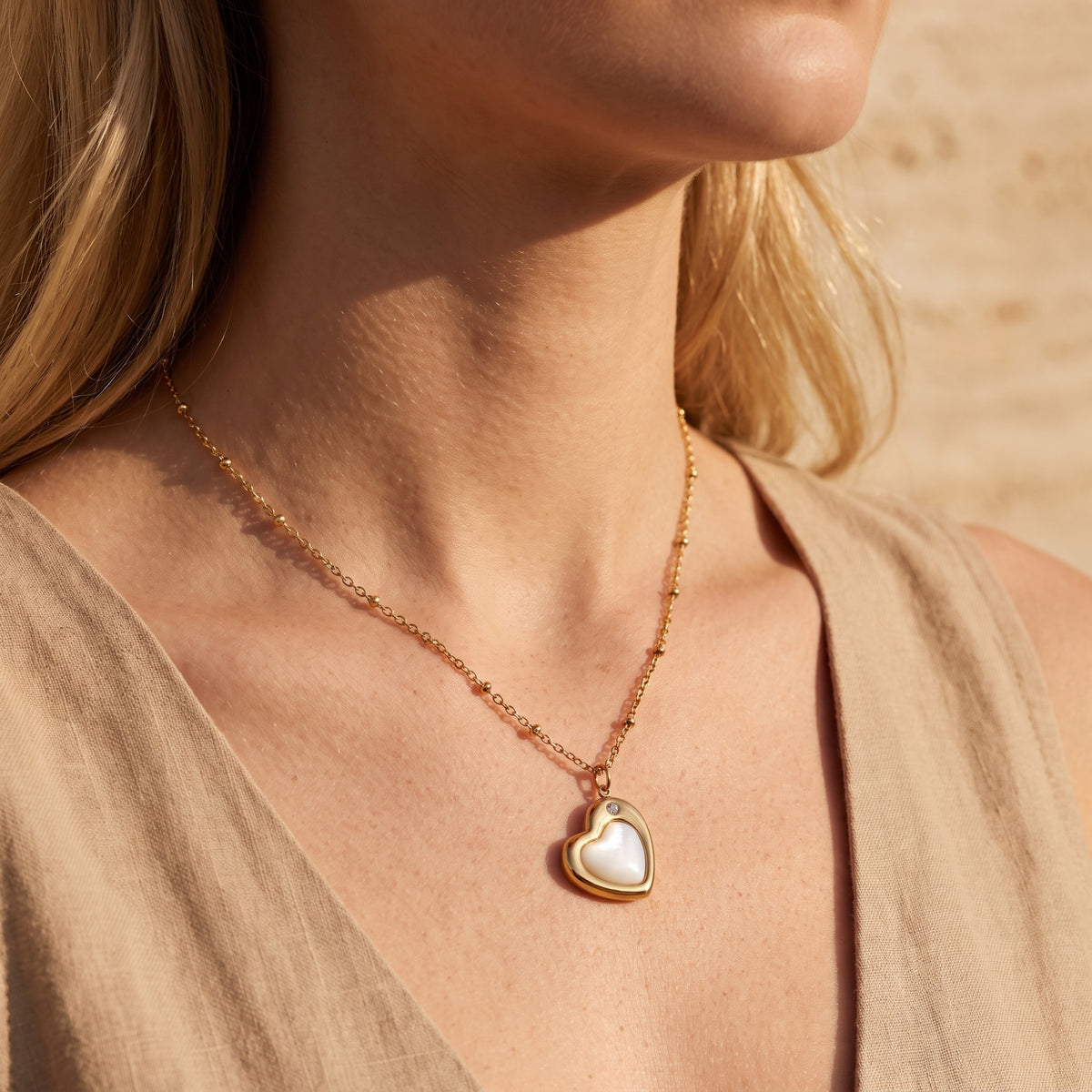 Close-up of a model wearing the gold-tone heart pendant necklace with a white insert and crystal accent over a beige top.