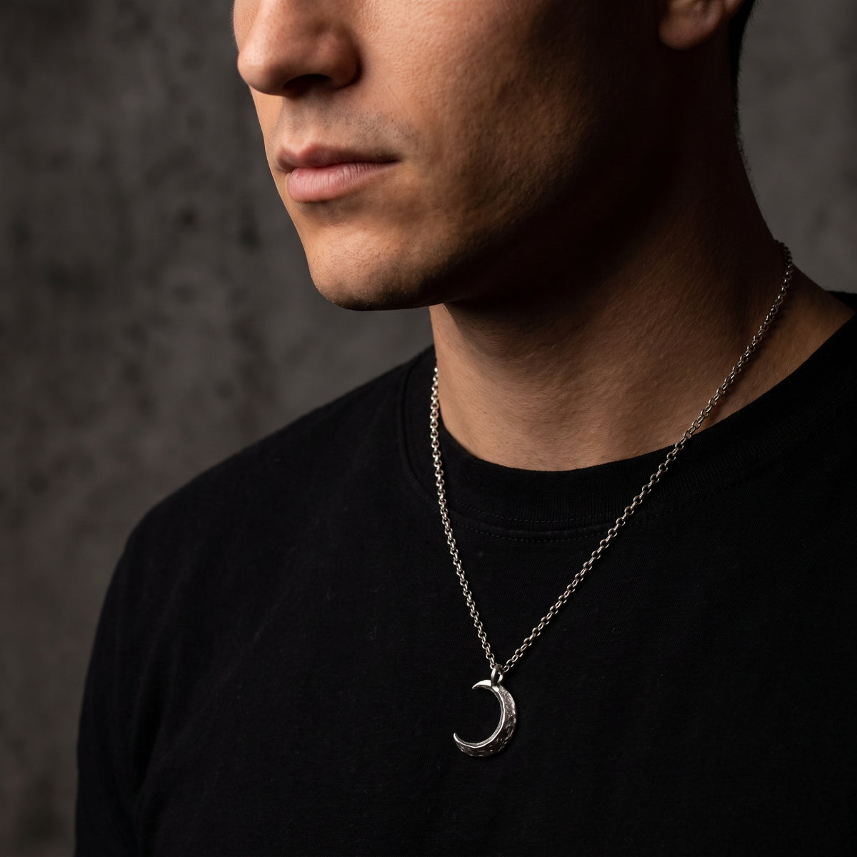 Front angle view of a man wearing the silver cratered moon pendant necklace over a black shirt.