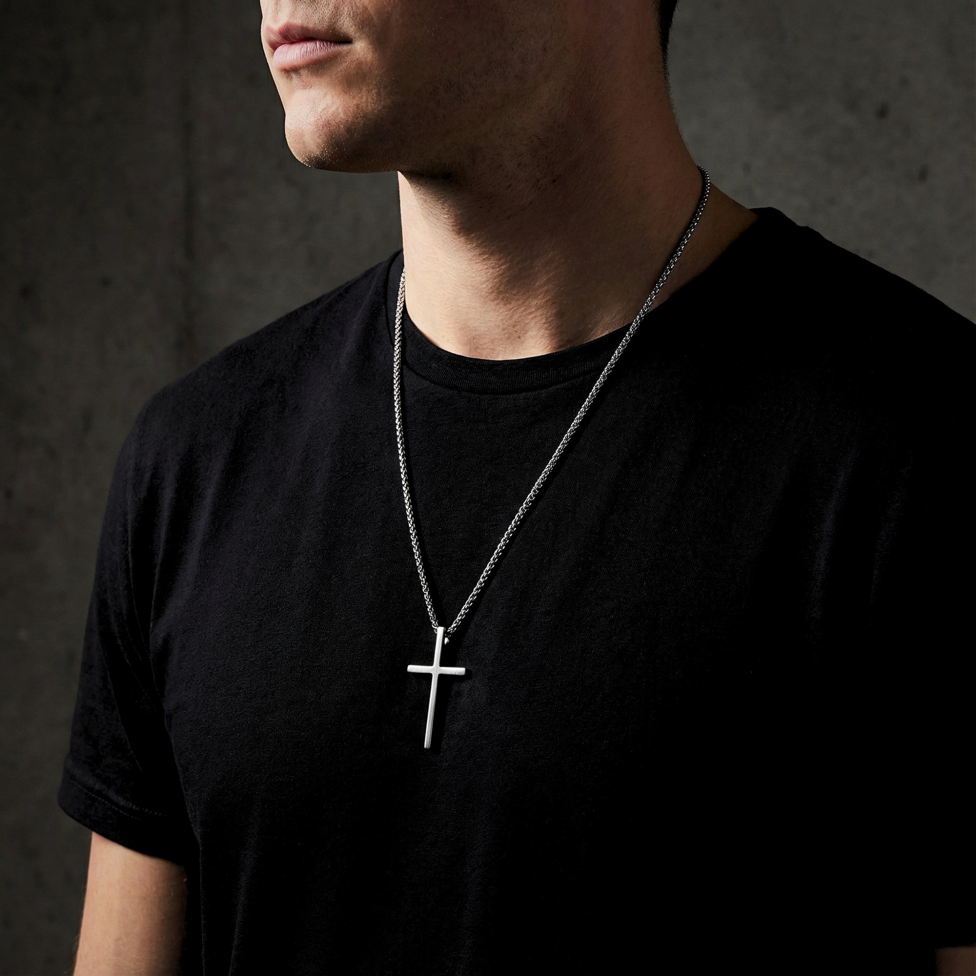 Silver stainless steel Devotion Cross pendant necklace worn by a man over a black t-shirt.