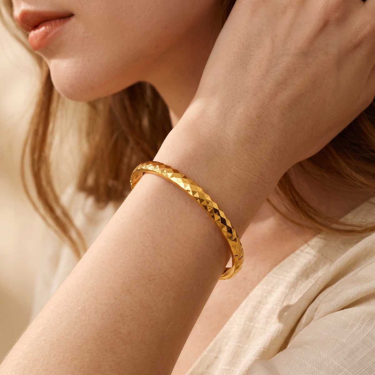 Close-up of a gold-toned faceted bangle bracelet worn on a wrist, with its hinged closure visible near the hand.