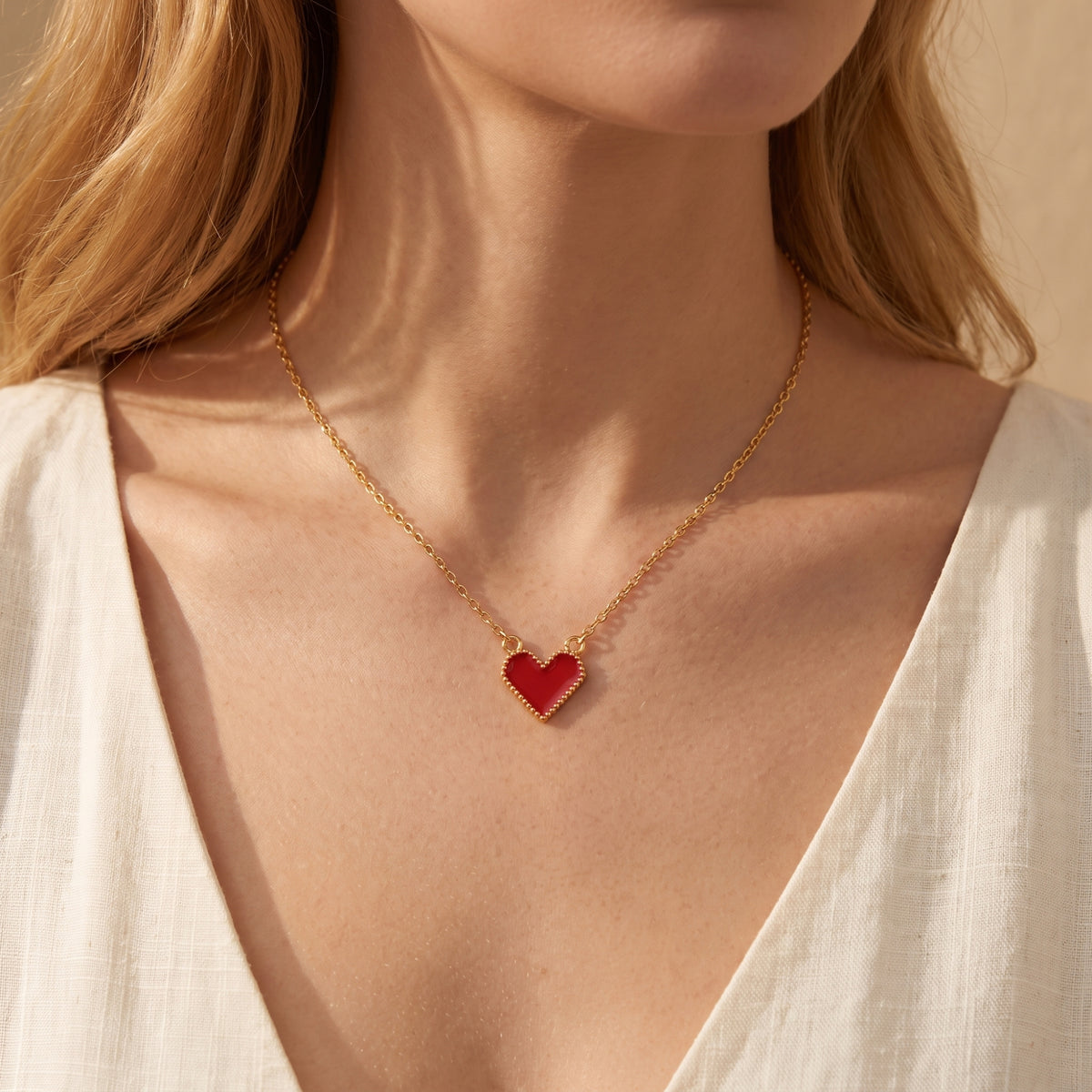 Front view of a model wearing the red heart pendant necklace over a white textured top.