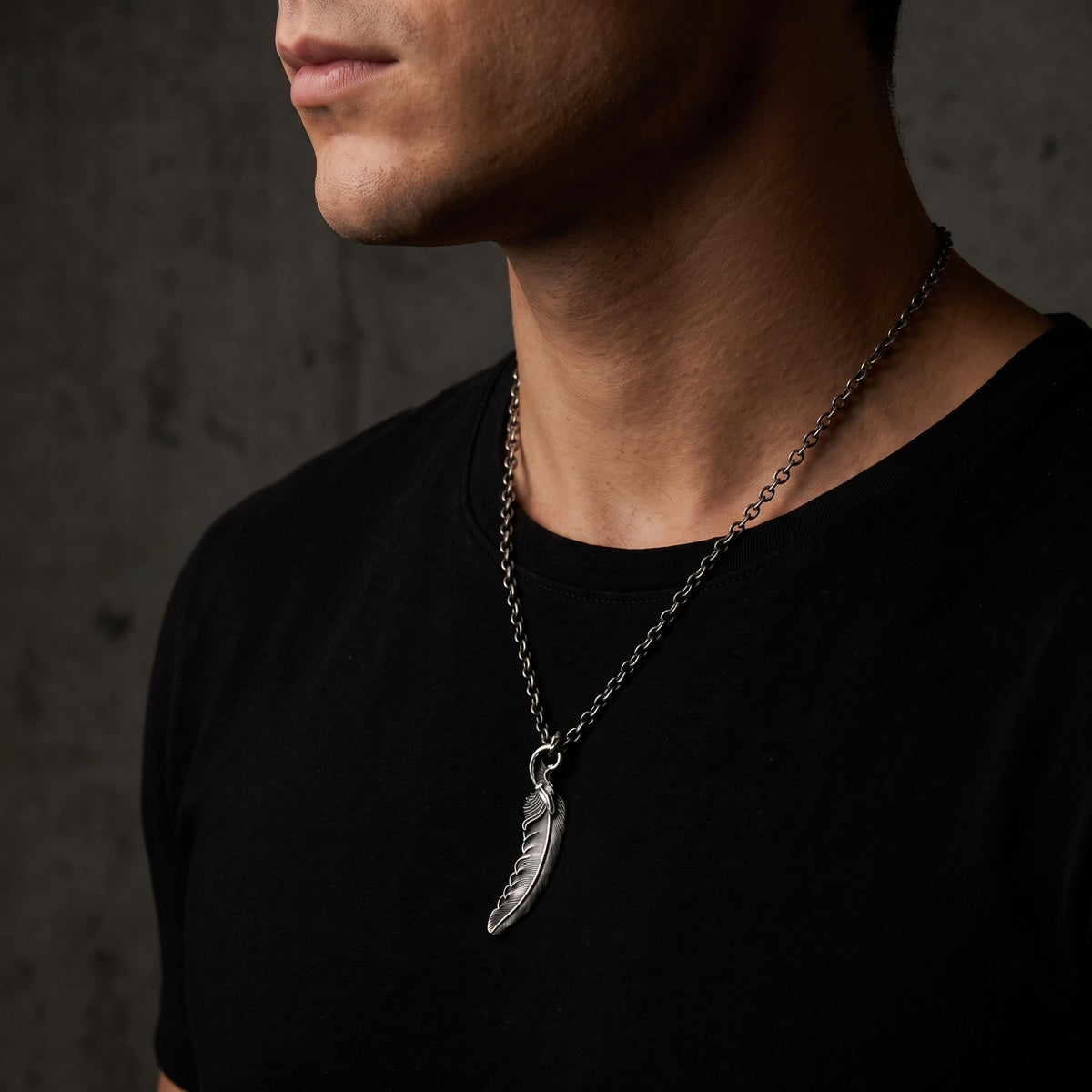 Side-angle view of a model wearing the silver feather pendant necklace over a black shirt.