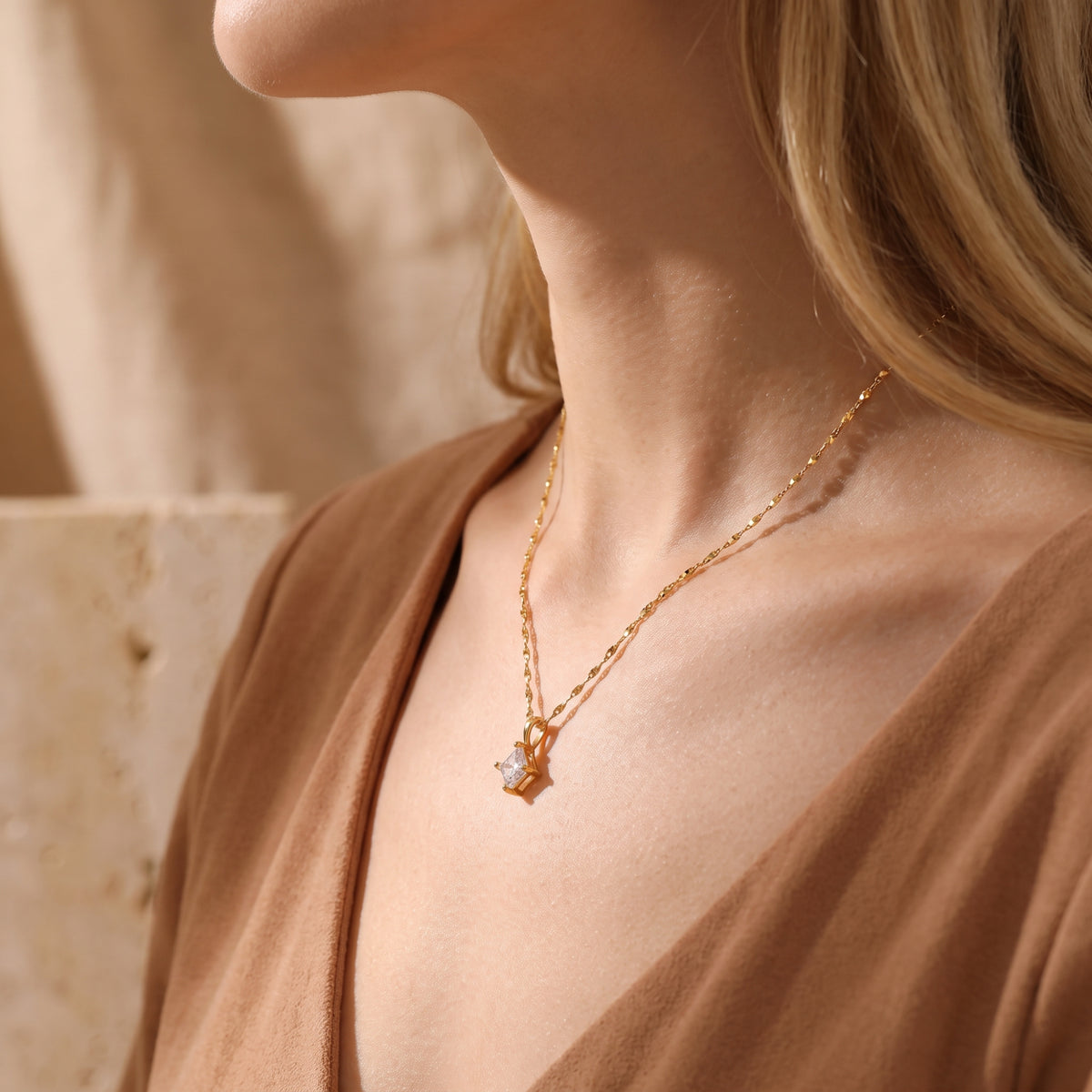 Gold-tone square solitaire pendant necklace worn over a light top with a brown open layer, shown from the side.