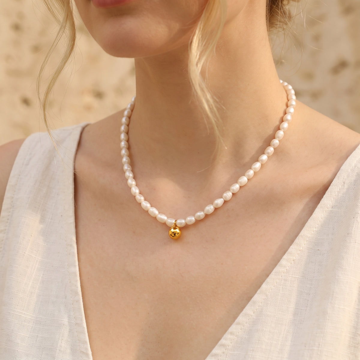 Front view of a model wearing a white pearl strand necklace with a centered gold-tone sphere pendant.