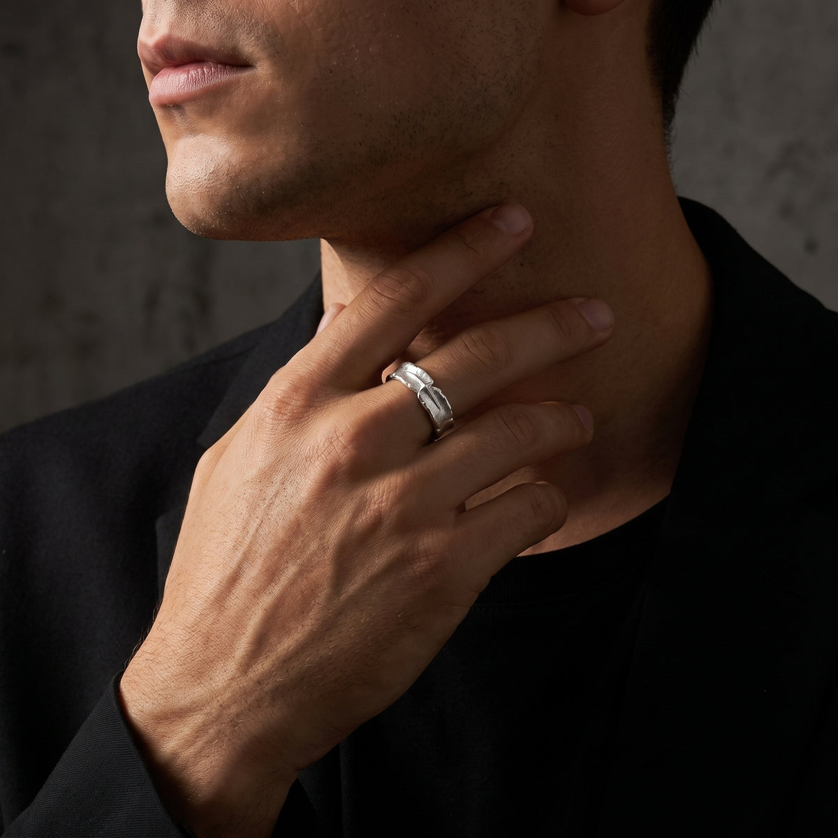 Close-up of a man wearing the chiseled silver starburst open-band ring while touching his neck.