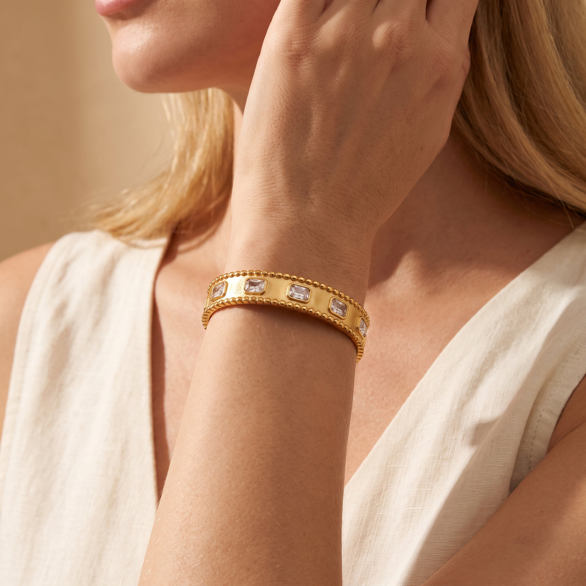 Wider view of a model wearing the gold-tone beaded cuff bracelet with clear stones against a light sleeveless top.