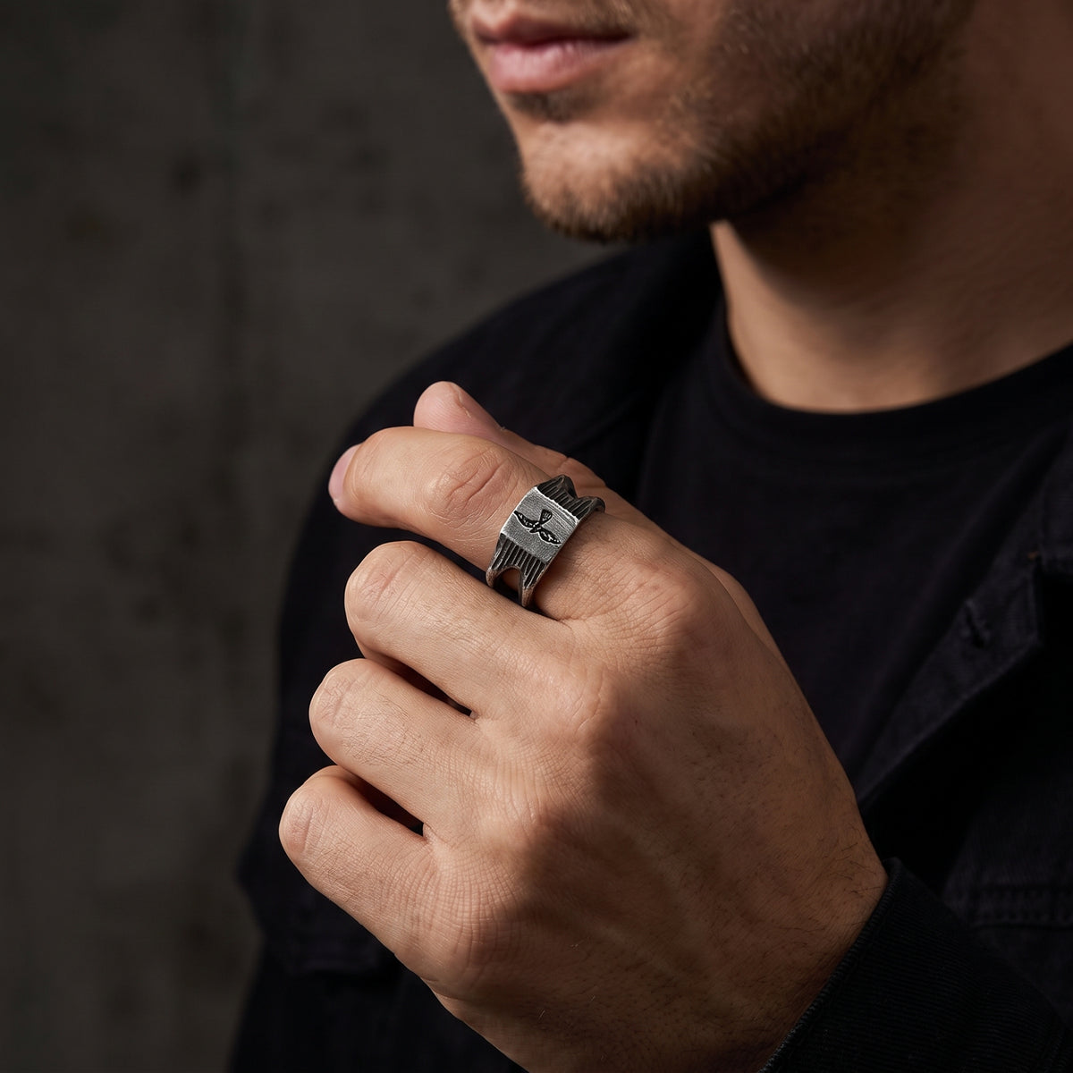 Close-up of a model wearing the textured silver falcon signet ring on his index finger.