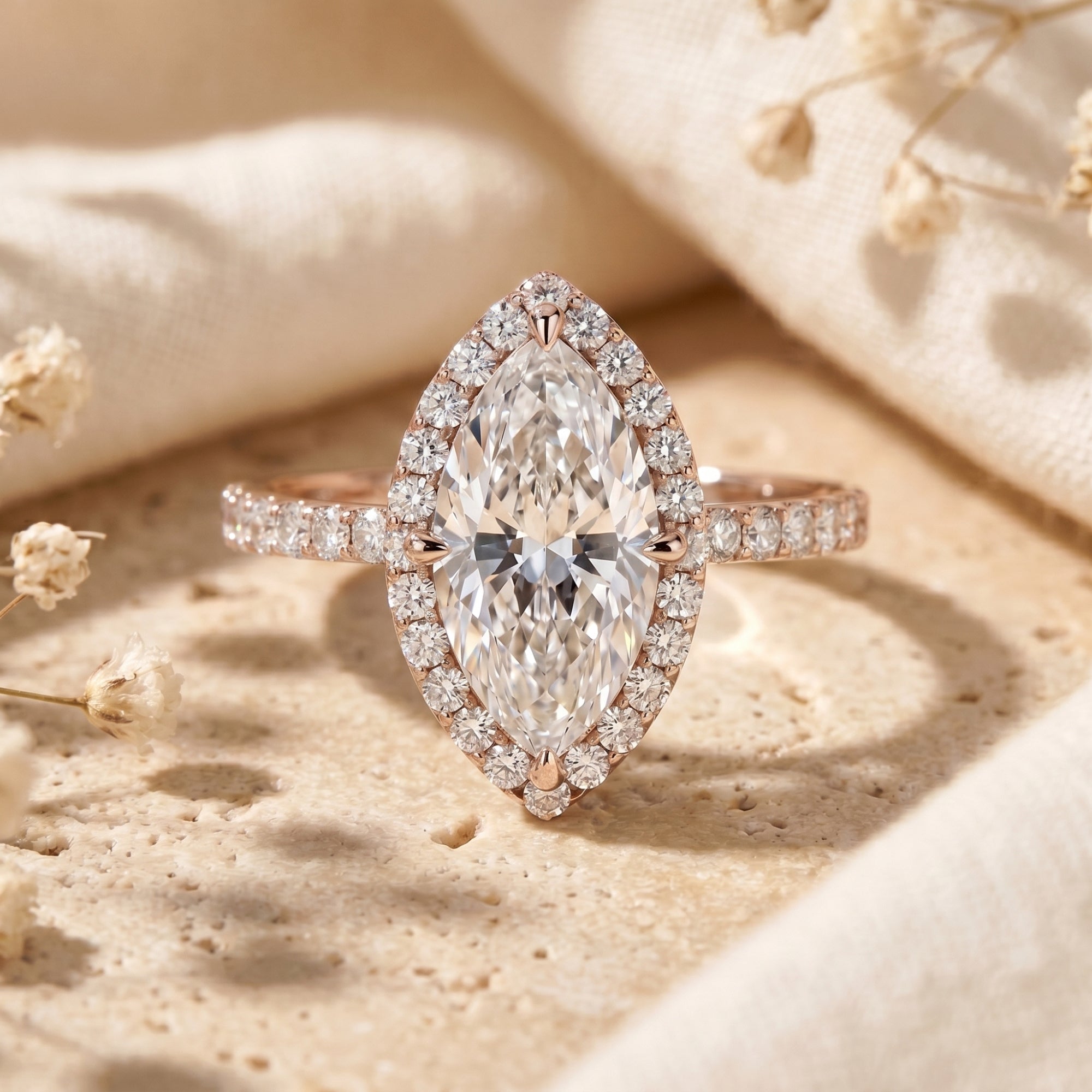 Rose gold marquise cut moissanite halo ring on a textured lifestyle surface.