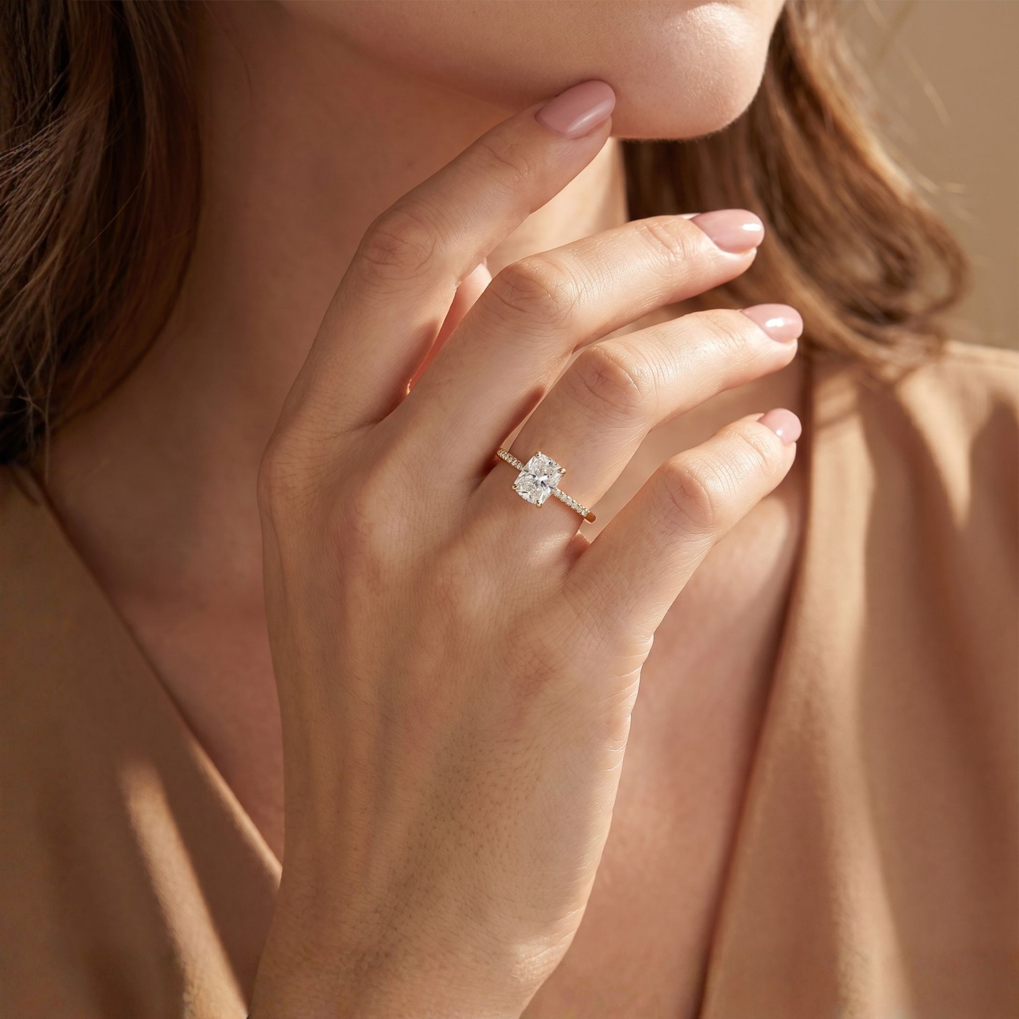 A close-up of a model's hand showcasing a brilliant cushion-cut moissanite ring set in yellow gold.