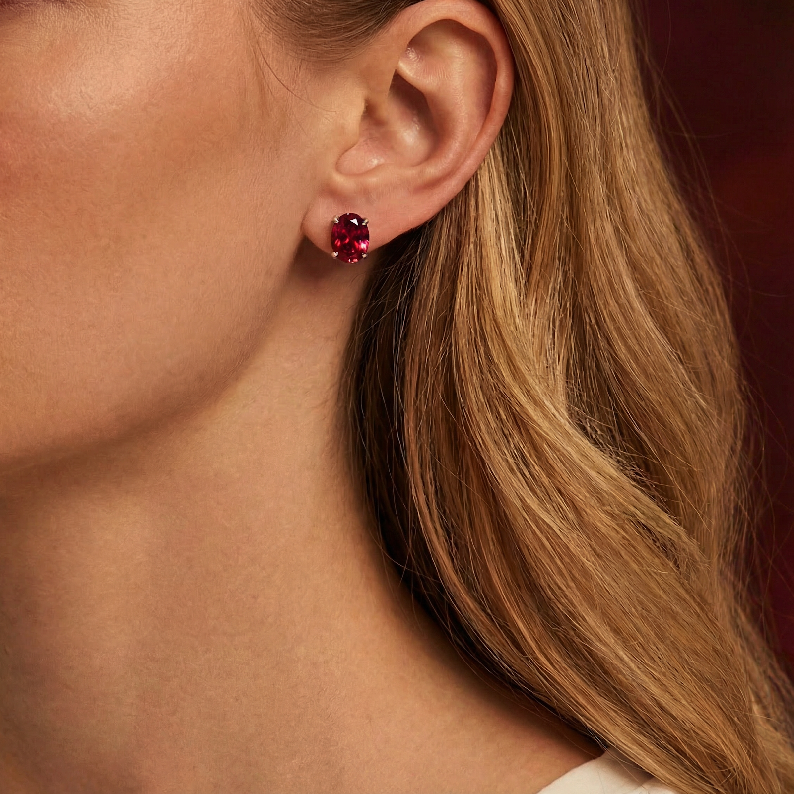 Woman wearing an oval-cut simulated ruby stud earring in sterling silver on her ear.