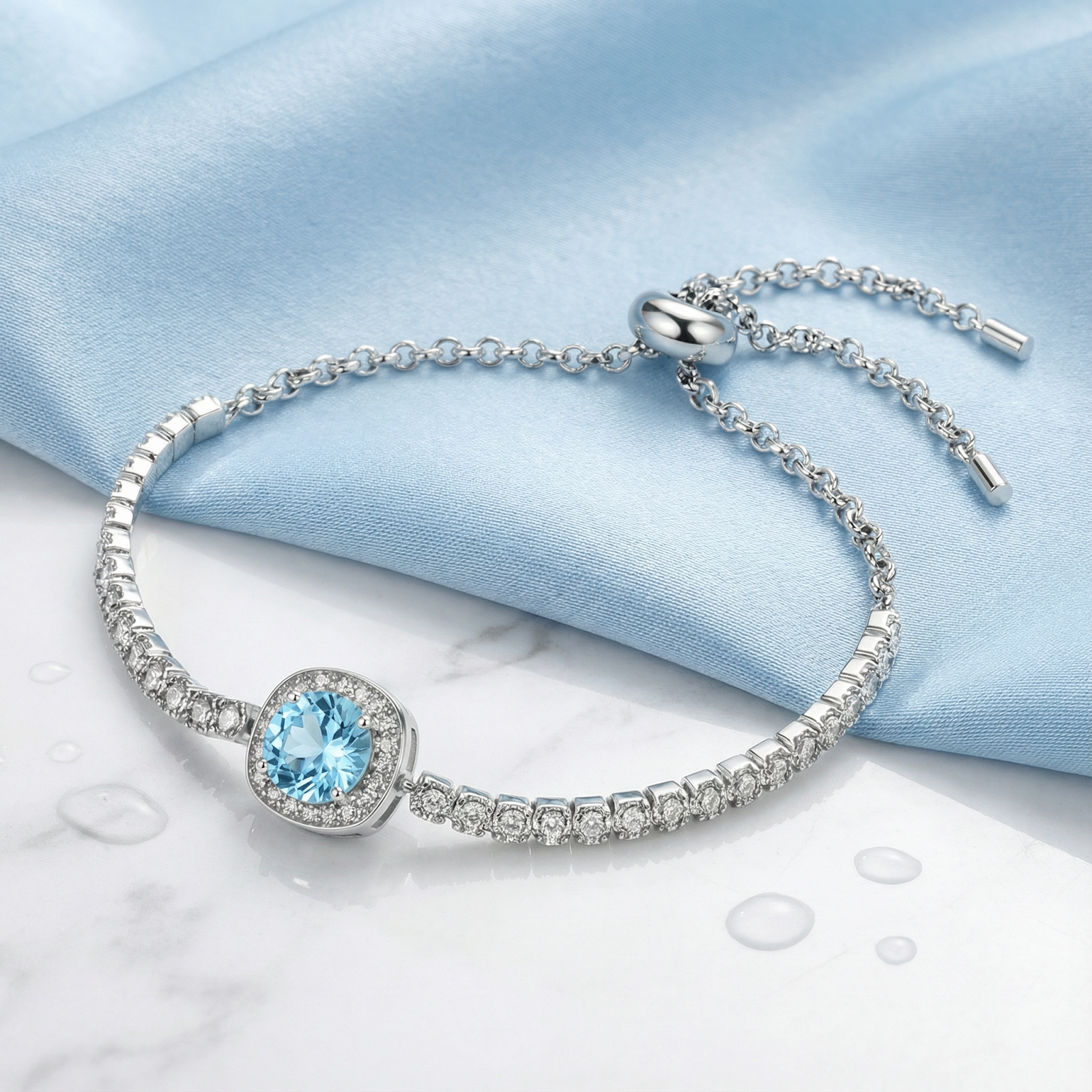 Sterling silver halo bracelet with a round simulated aquamarine on a blue fabric and marble background.