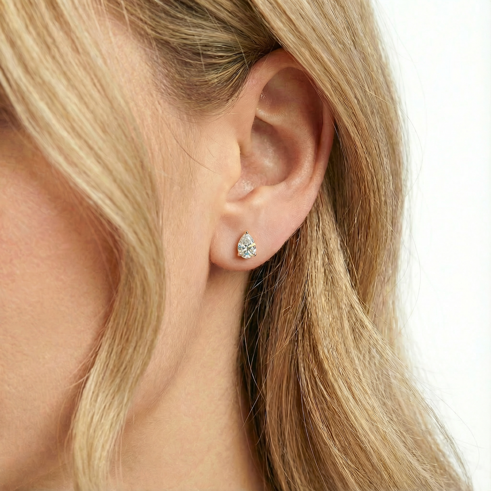 Close-up of a pear-cut simulated diamond stud earring in 18K gold vermeil worn on a woman's ear.